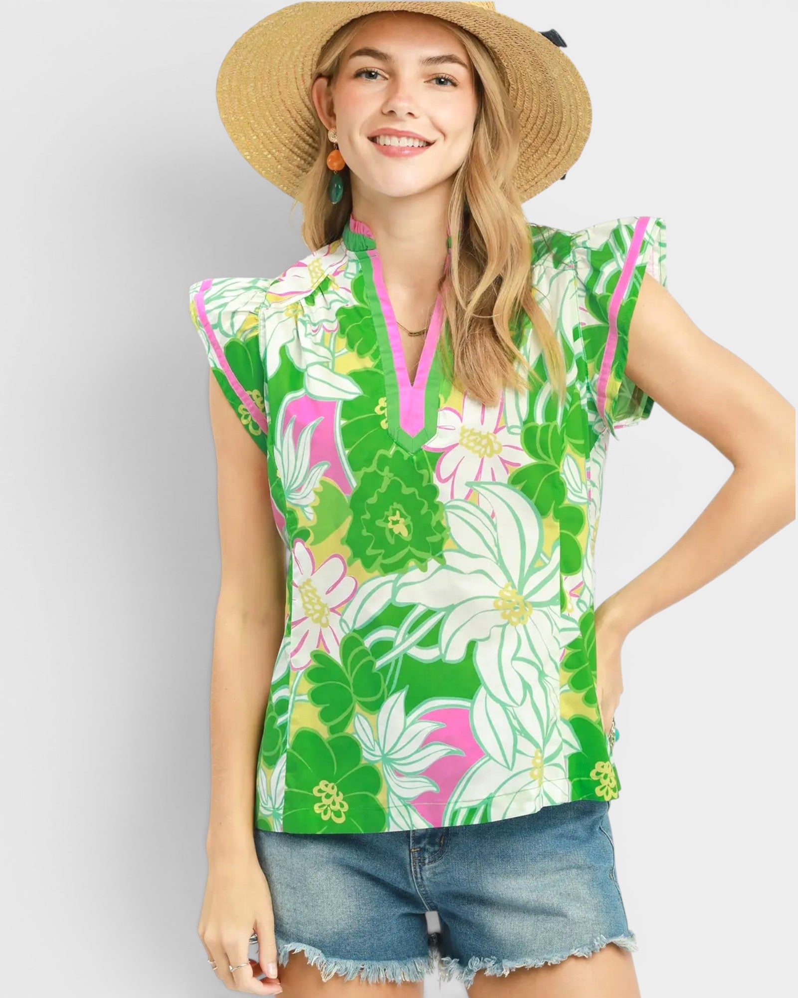 Woman wearing a green floral sleeveless top and denim shorts on a white background