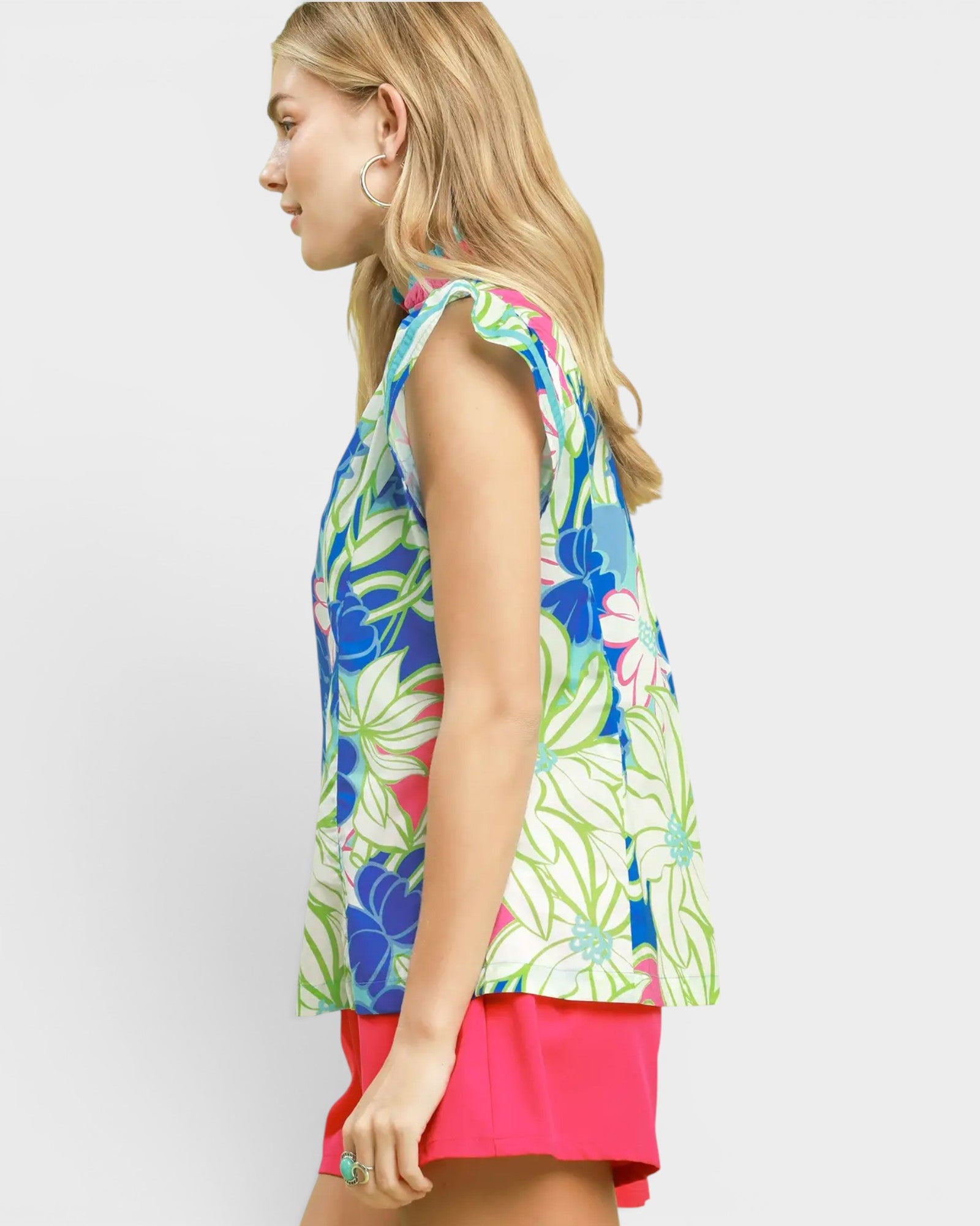 Woman wearing a colorful floral sleeveless top and pink shorts on a white background