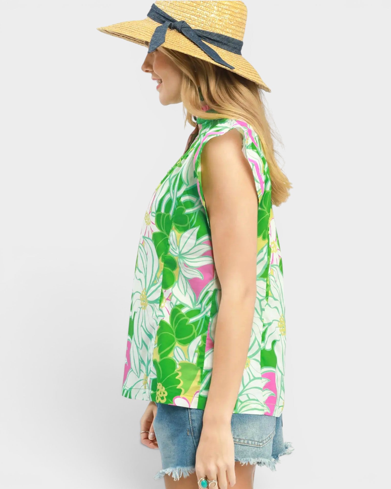 Woman wearing a colorful sleeveless top with floral pattern and a straw hat on a white background