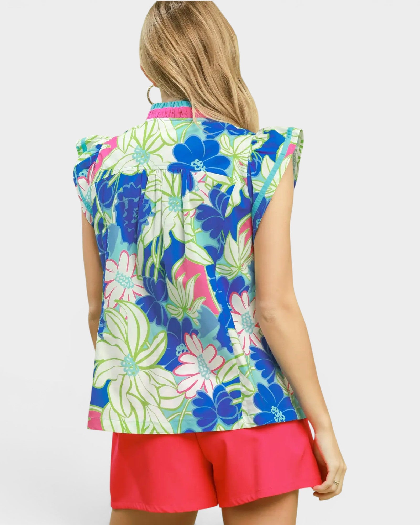 Woman wearing a colorful floral sleeveless top and pink shorts on a white background