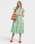 Woman wearing a colorful floral dress holding a woven bag on a white background
