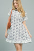 Woman wearing a white dress with black floral pattern against a gray background
