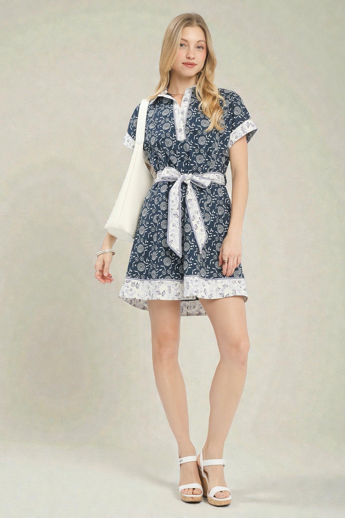 Woman wearing a blue patterned dress with a white belt on a plain background