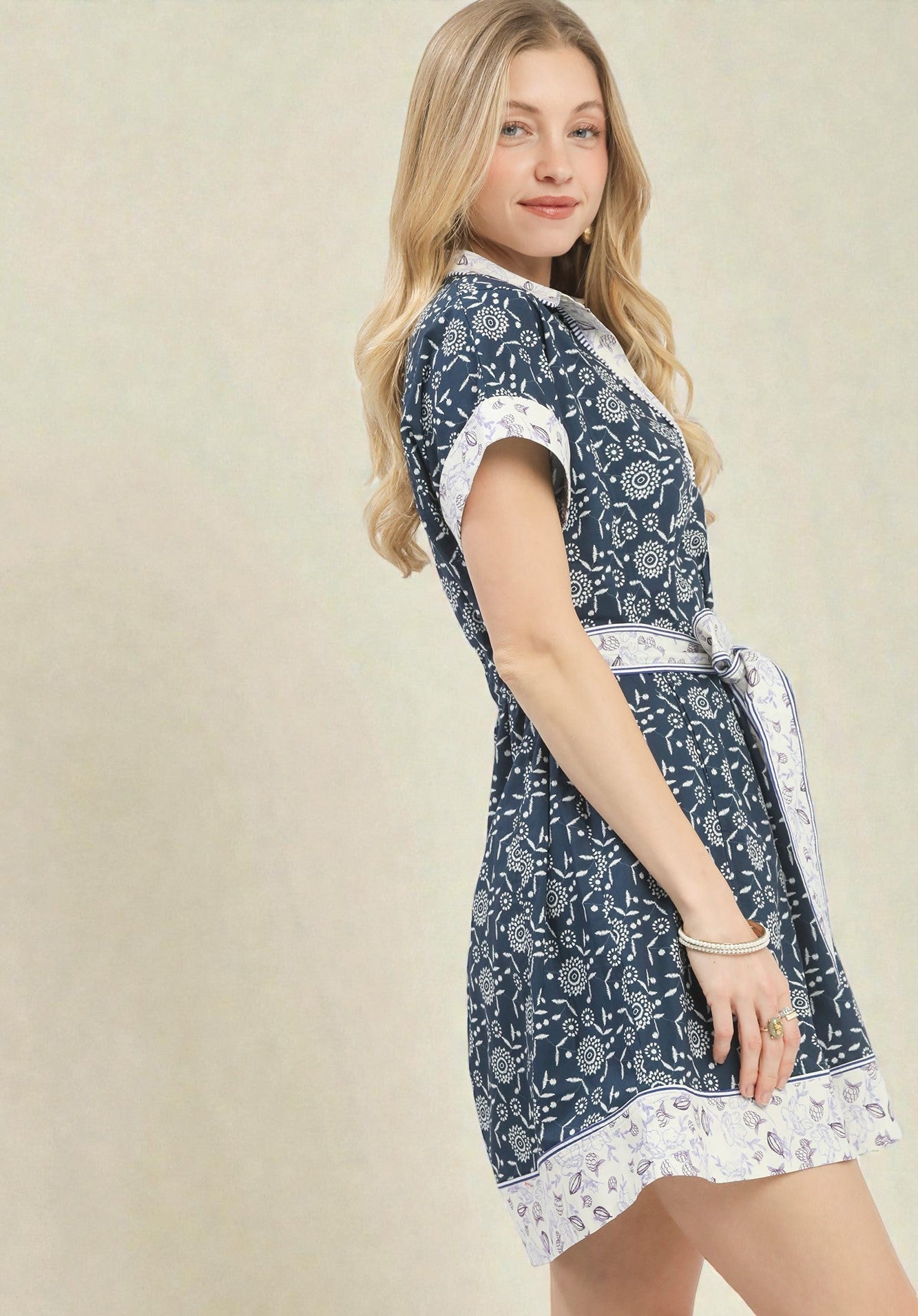 Woman wearing a navy patterned dress with white accents on a beige background