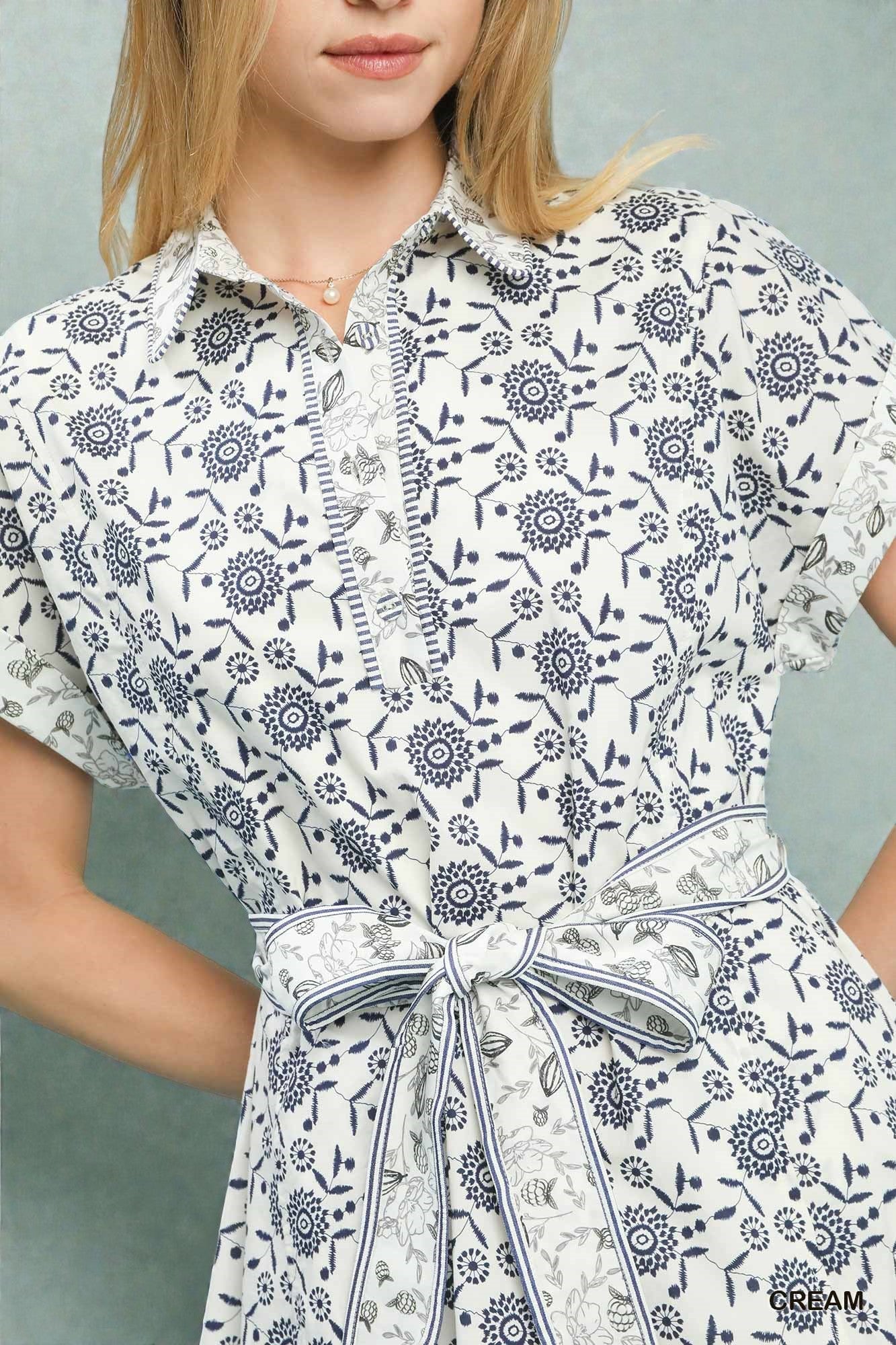 Woman wearing a white dress with black floral pattern against a gray background