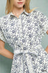 Woman wearing a white dress with black floral pattern against a gray background