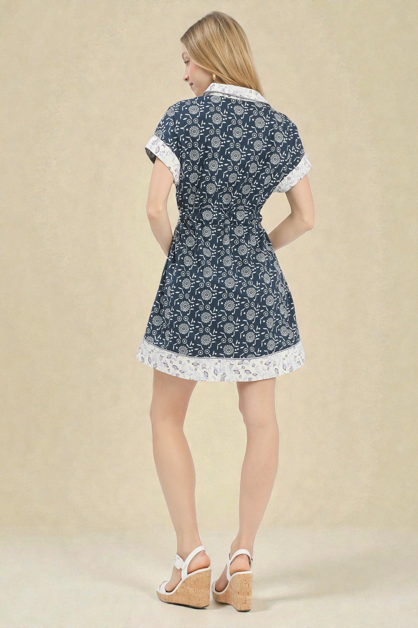 Woman wearing a blue floral dress with white trim on a beige background