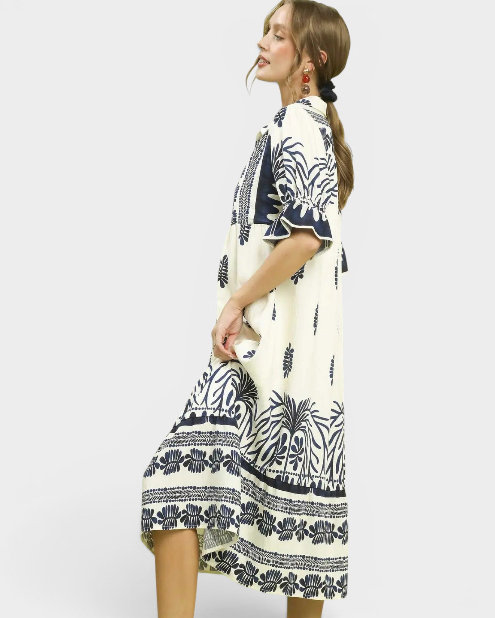 Woman wearing a white dress with black floral patterns on a plain background