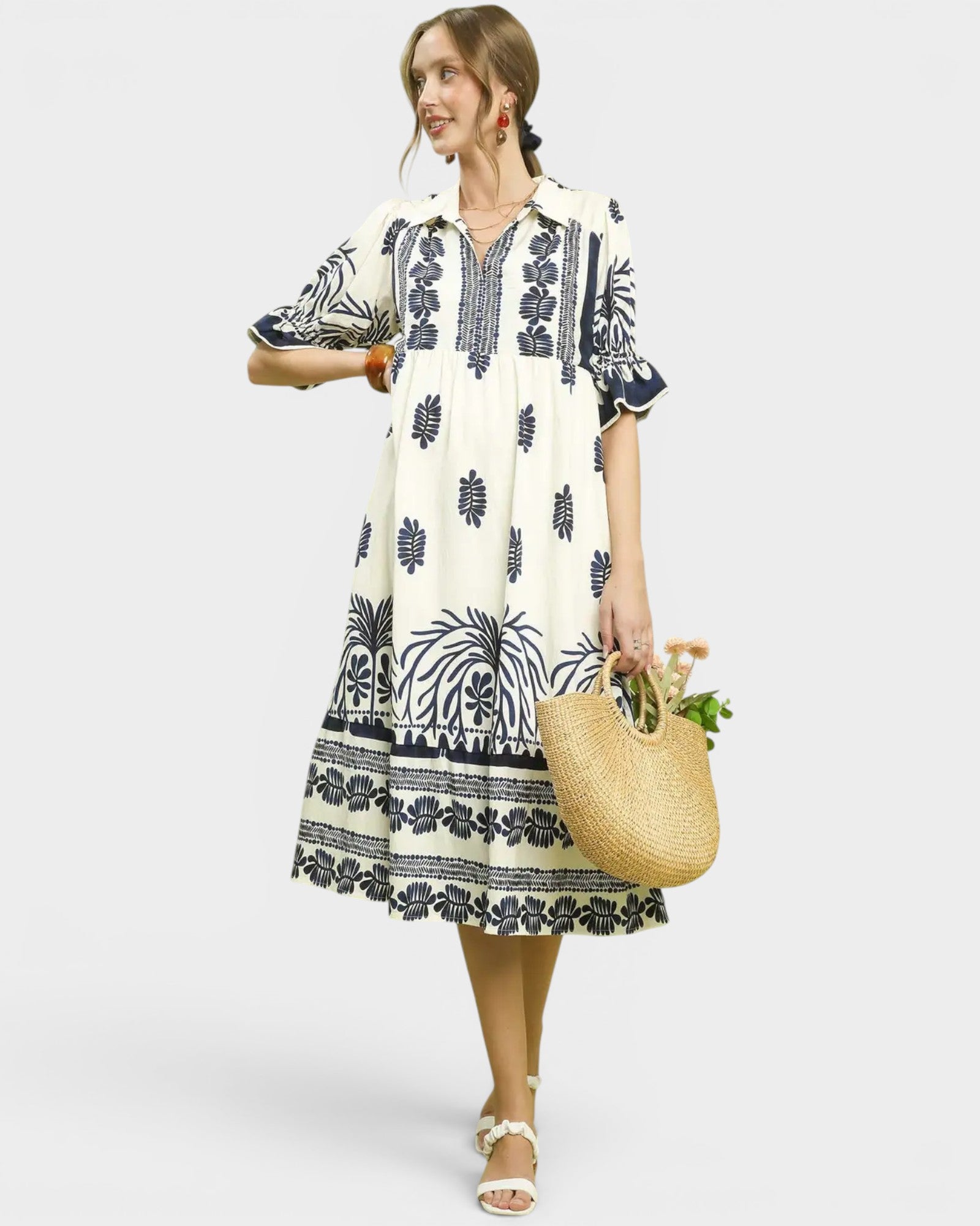 Woman wearing a white dress with black patterns, holding a woven bag and flowers, on a white background