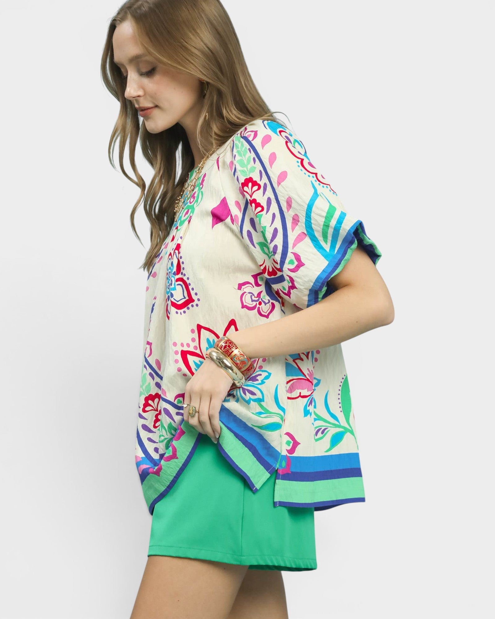 Woman wearing a colorful patterned top and green shorts on a white background