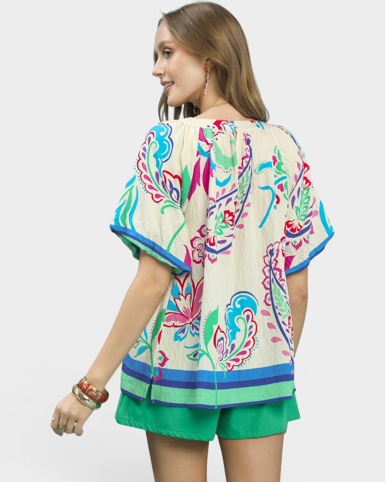 Woman wearing a colorful floral kimono-style top with green shorts on a white background