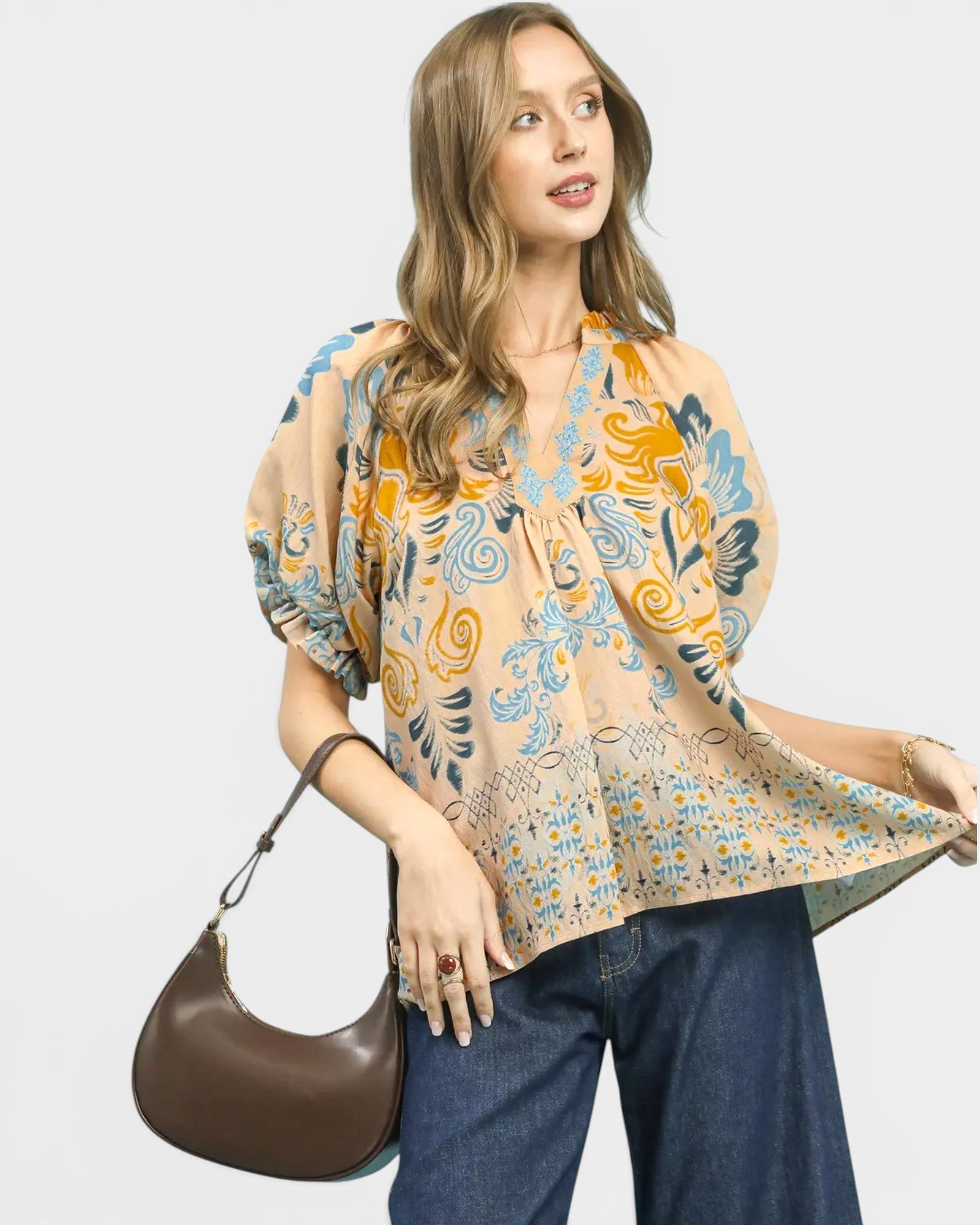 Woman wearing a patterned blouse and holding a brown handbag on a white background