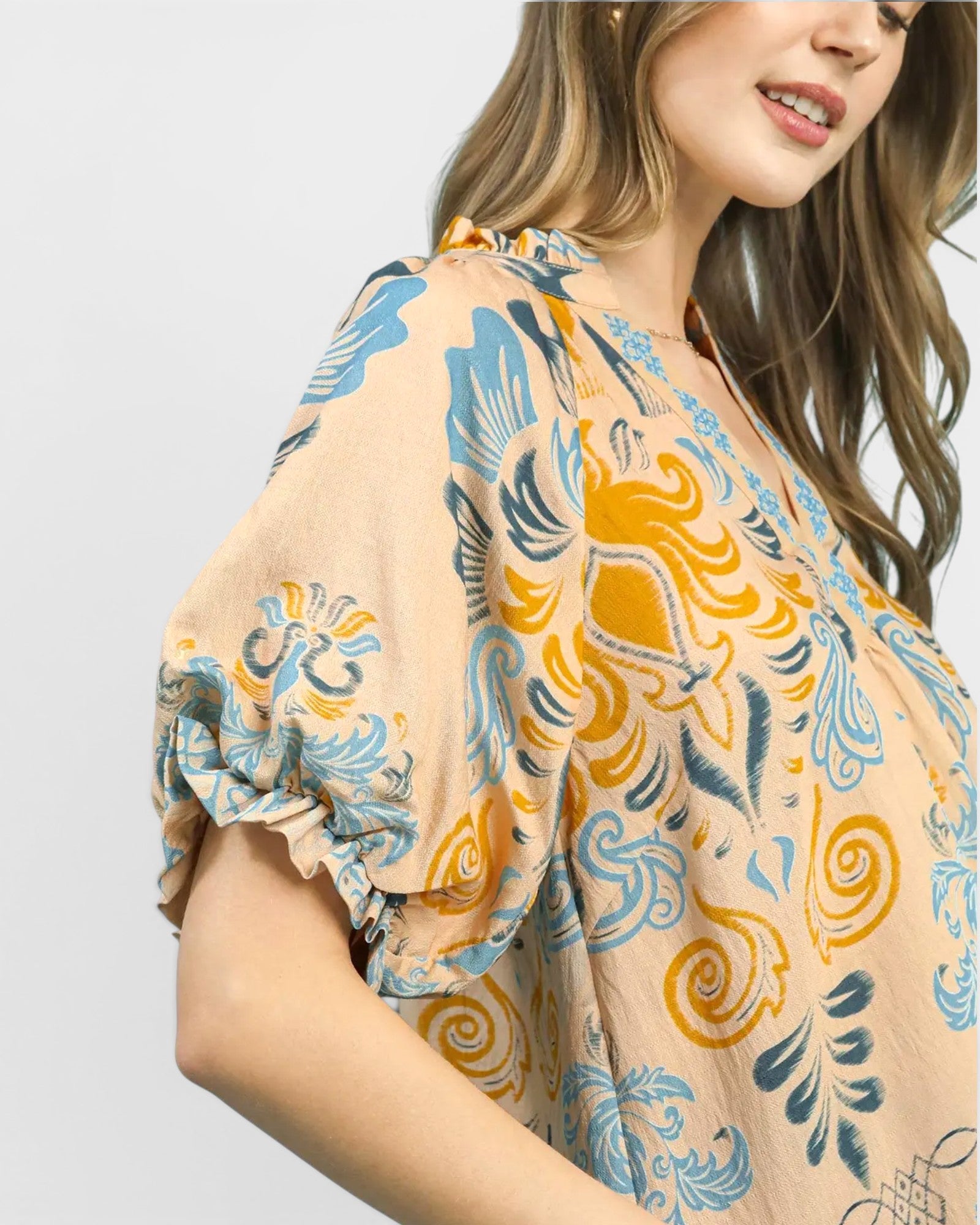 Woman wearing a patterned blouse with blue and yellow designs on a plain background