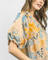 Woman wearing a patterned blouse with blue and yellow designs on a plain background
