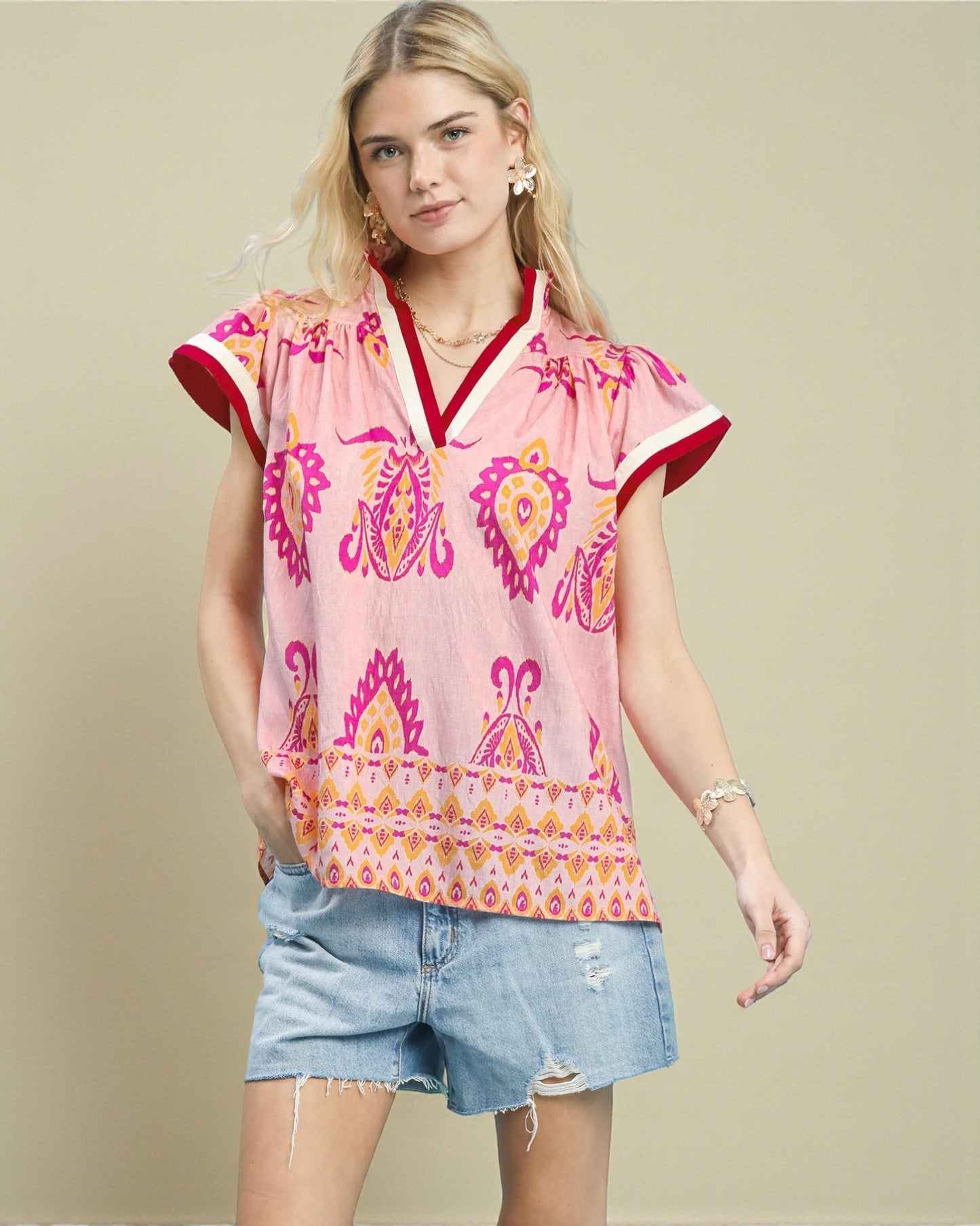 Woman wearing a pink patterned top and denim shorts on a beige background