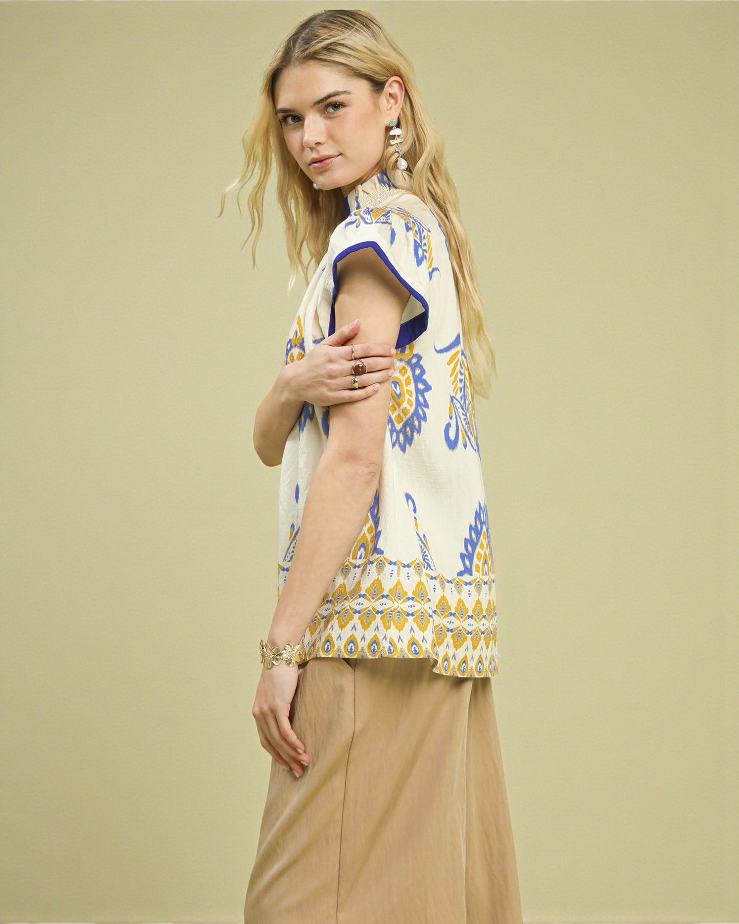 Woman wearing a patterned top and beige pants against a plain background