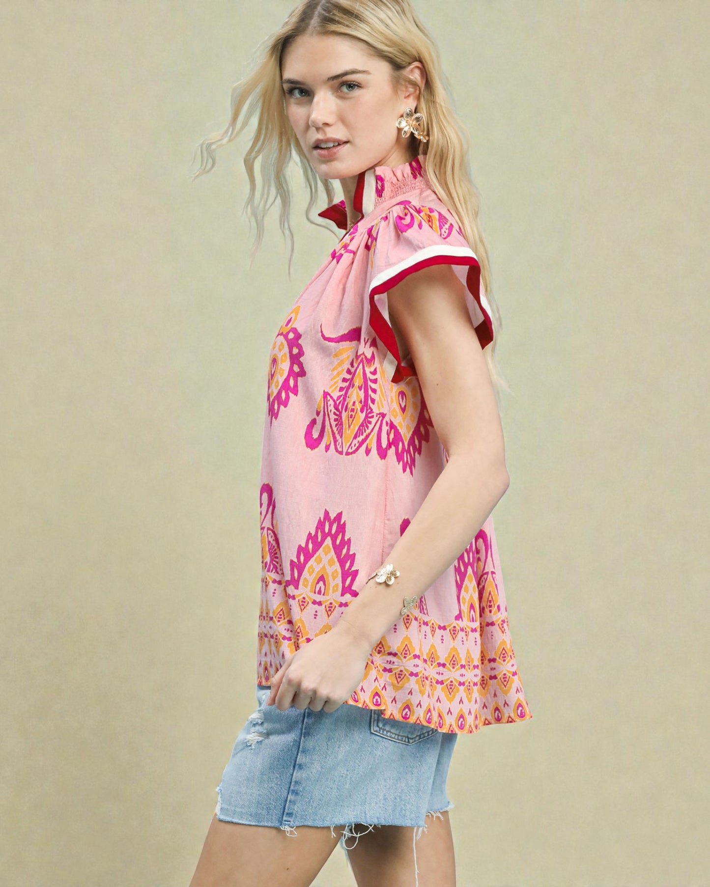 Woman wearing a pink patterned top and denim shorts on a beige background