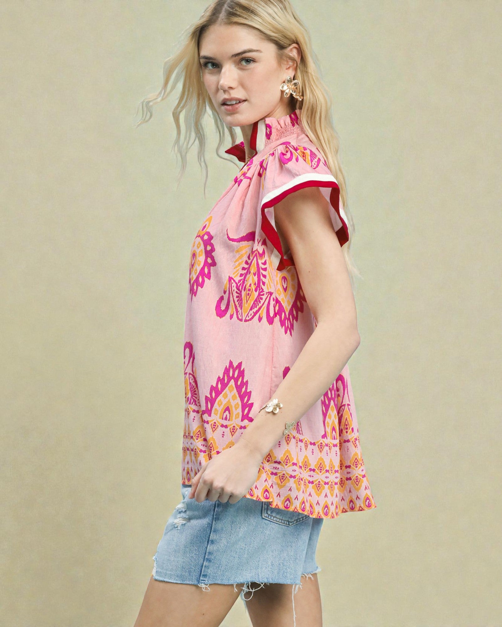 Woman wearing a pink patterned top and denim shorts on a beige background