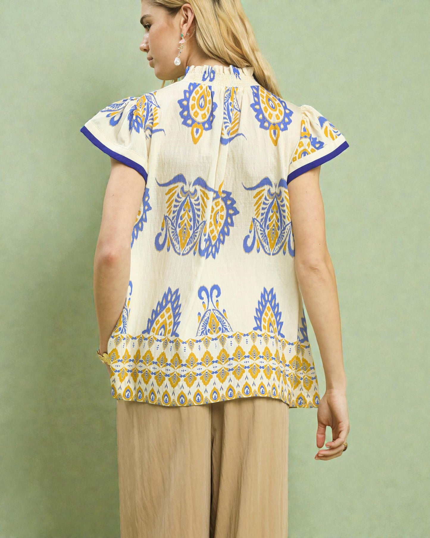 Woman wearing a patterned top with short sleeves on a green background