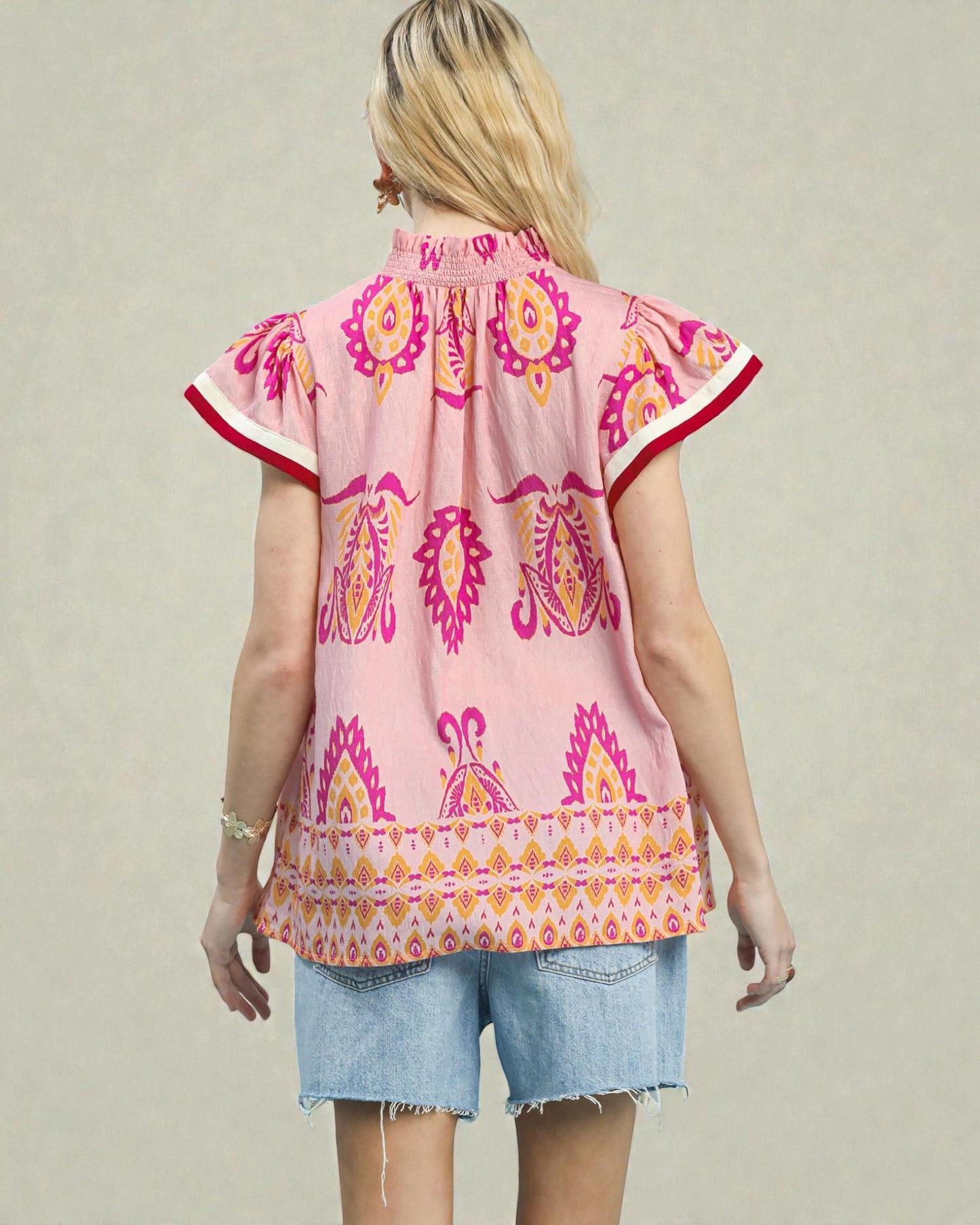 Woman wearing a pink patterned top with short sleeves on a plain background