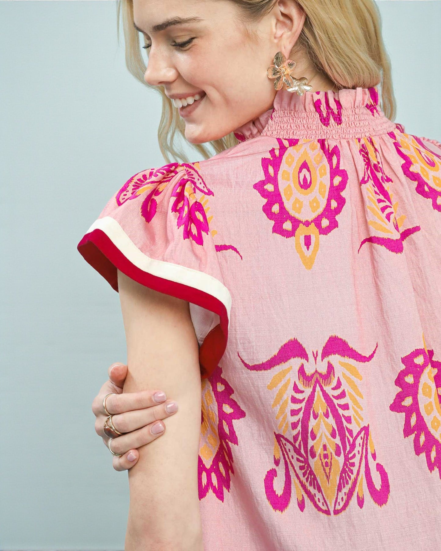 Woman wearing a pink dress with colorful patterns on a light blue background