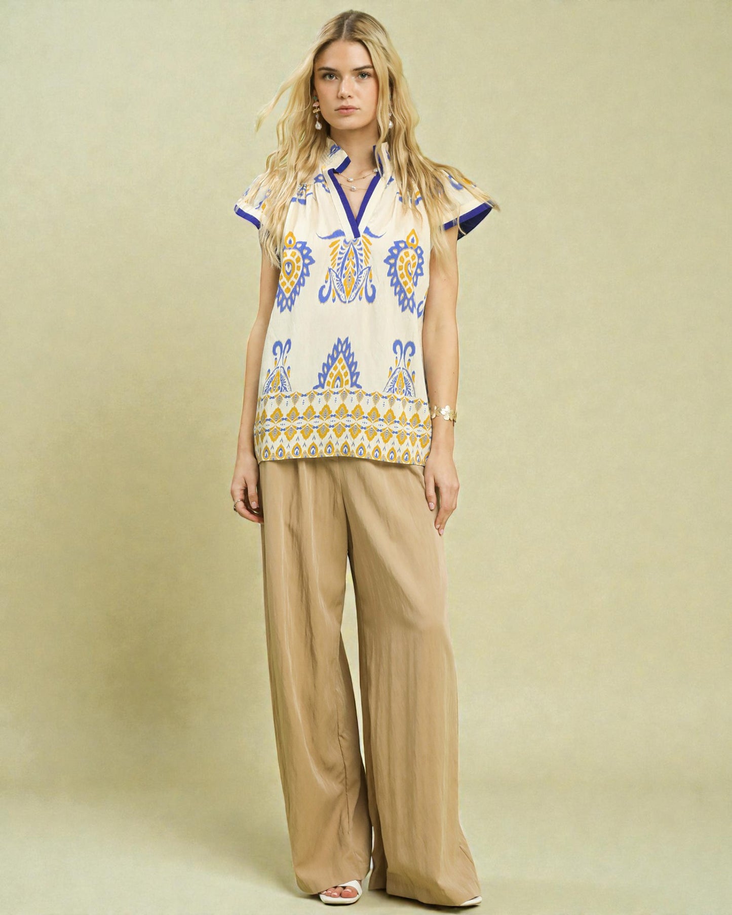 Woman wearing a patterned top and beige pants against a beige background