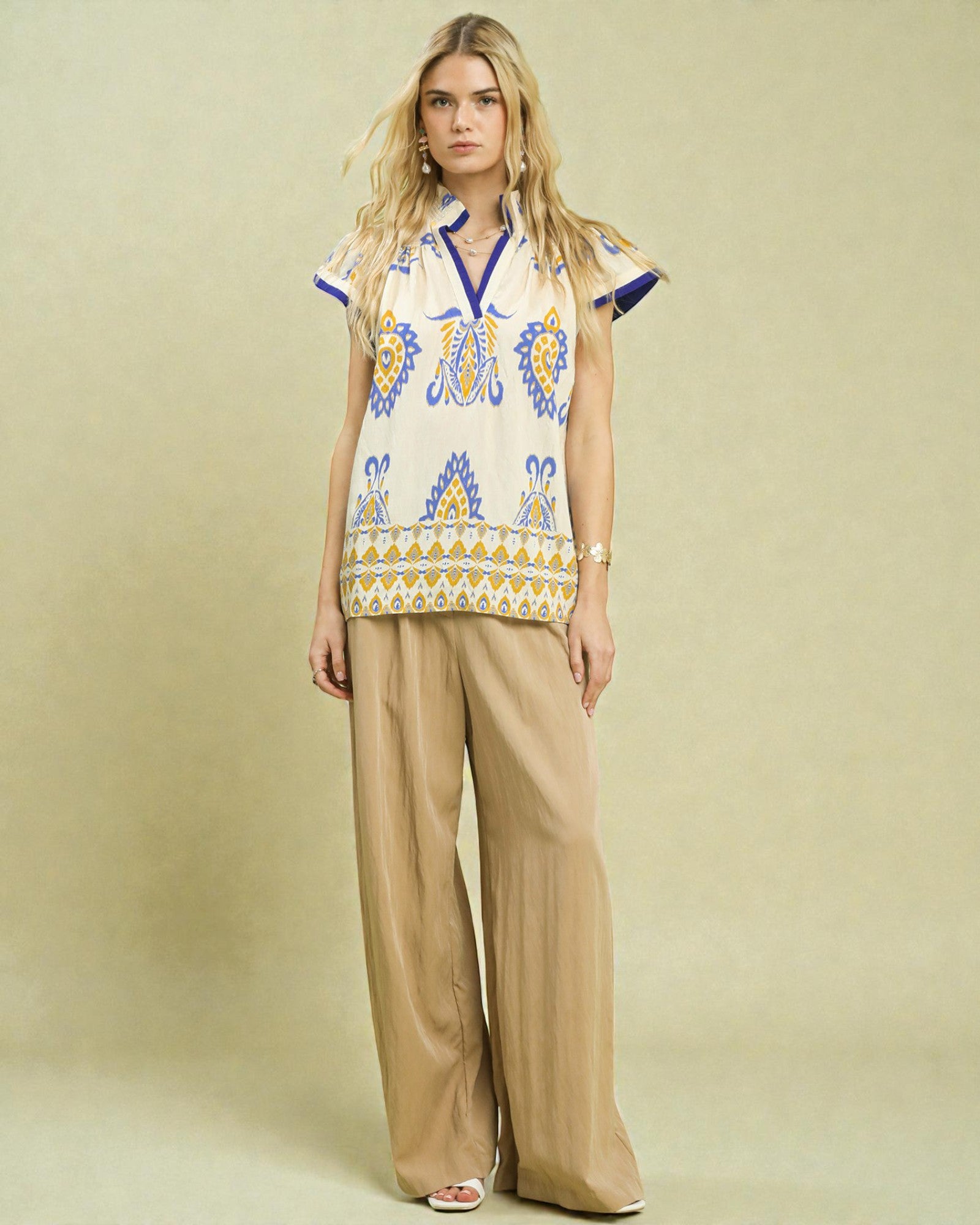 Woman wearing a patterned top and beige pants against a beige background