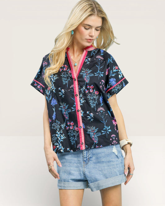 Woman wearing a floral patterned shirt with pink accents on a plain background