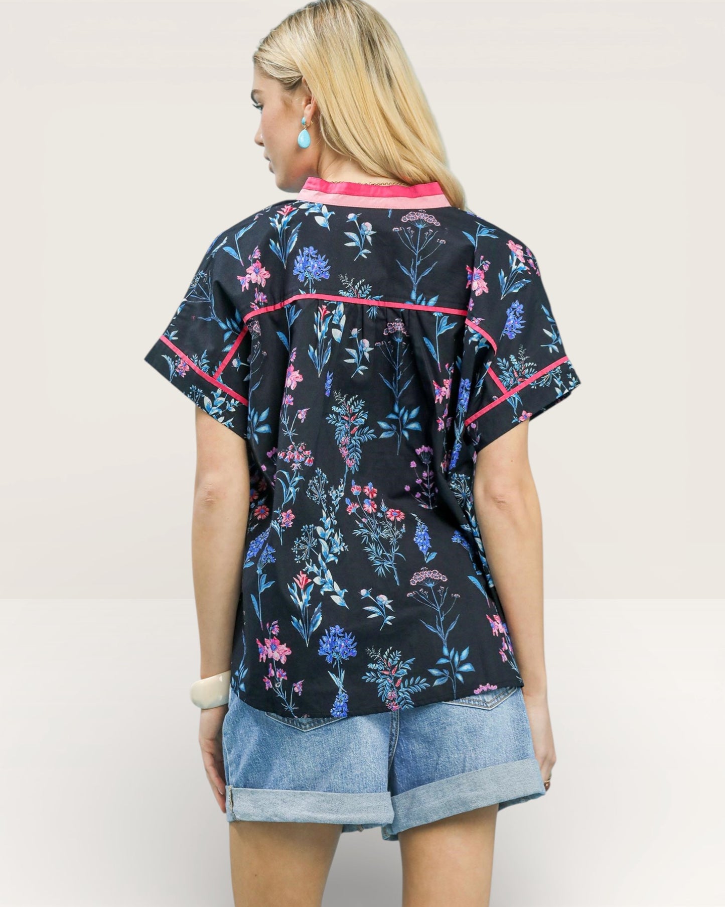 Woman wearing a black floral patterned shirt with pink accents on a plain background