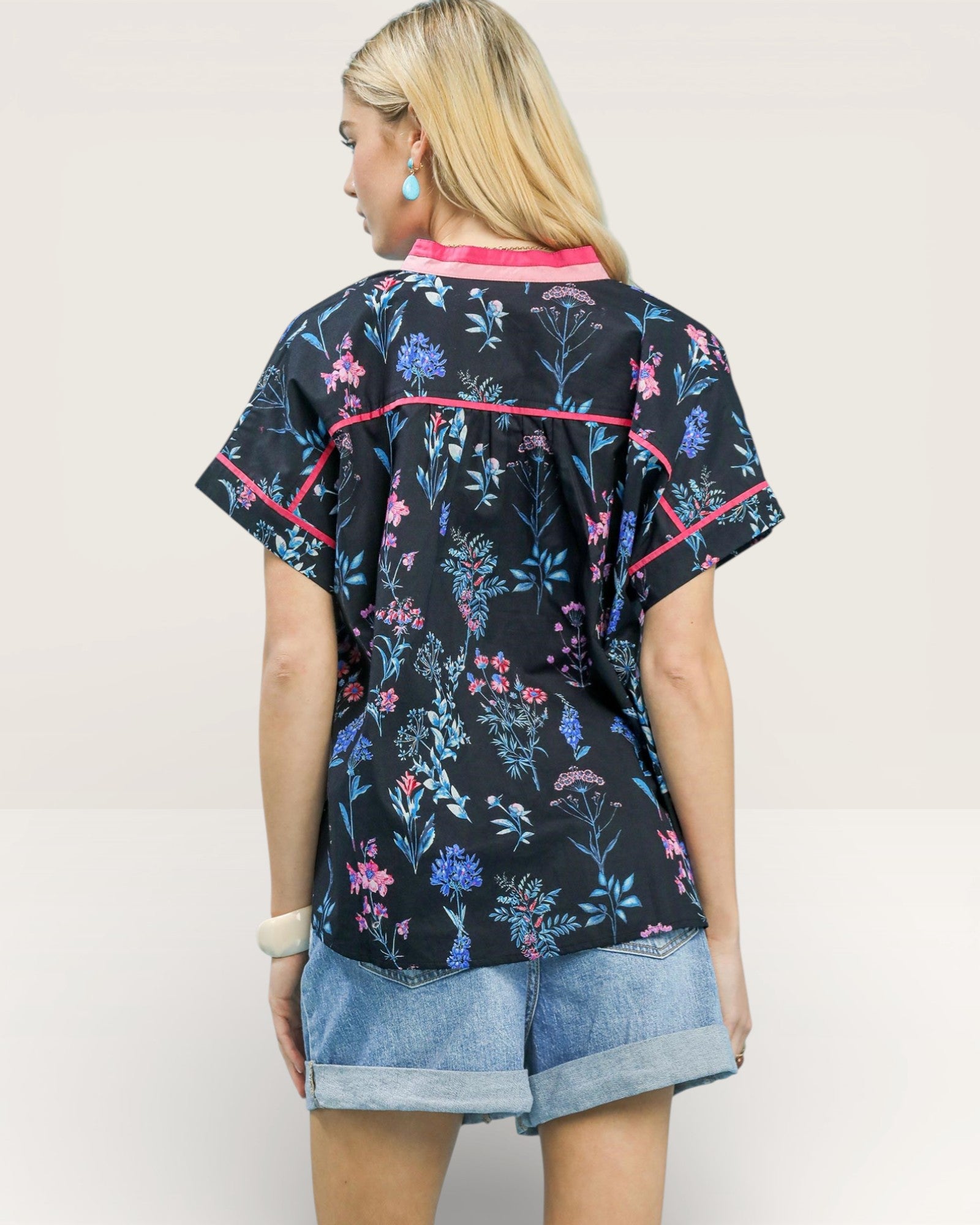 Woman wearing a black floral patterned shirt with pink accents on a plain background