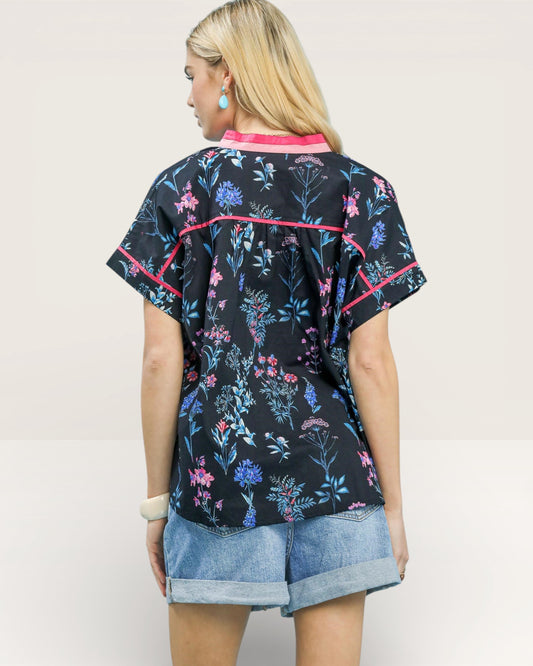 Woman wearing a black floral patterned shirt with pink accents on a plain background