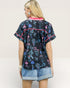 Woman wearing a black floral patterned shirt with pink accents on a plain background