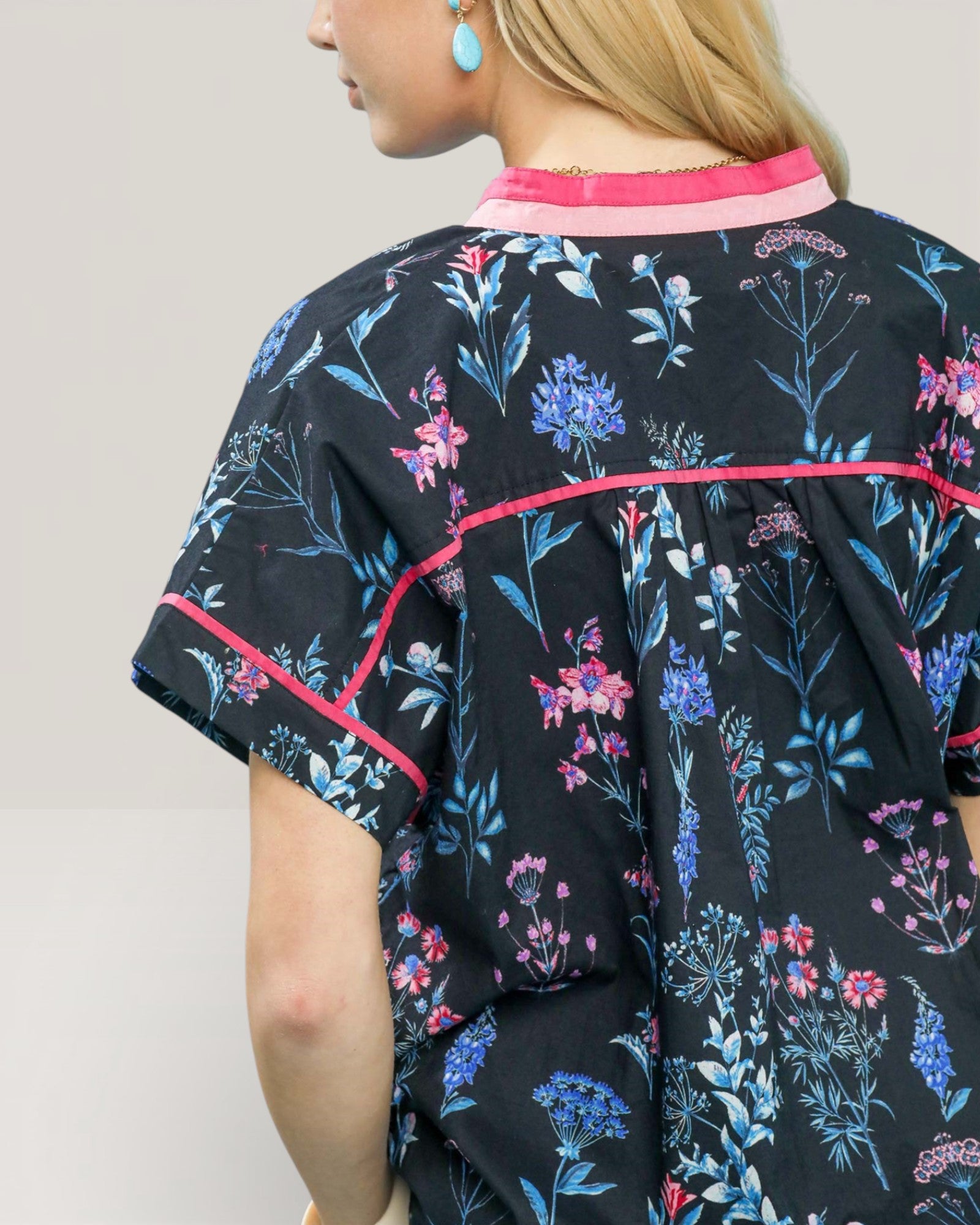 Person wearing a black floral dress with pink trim on a plain background