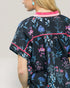 Person wearing a black floral dress with pink trim on a plain background