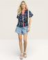 Woman wearing a floral blouse and denim shorts on a white background