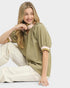 Woman wearing a green ribbed sweater and white pants sitting on a white background