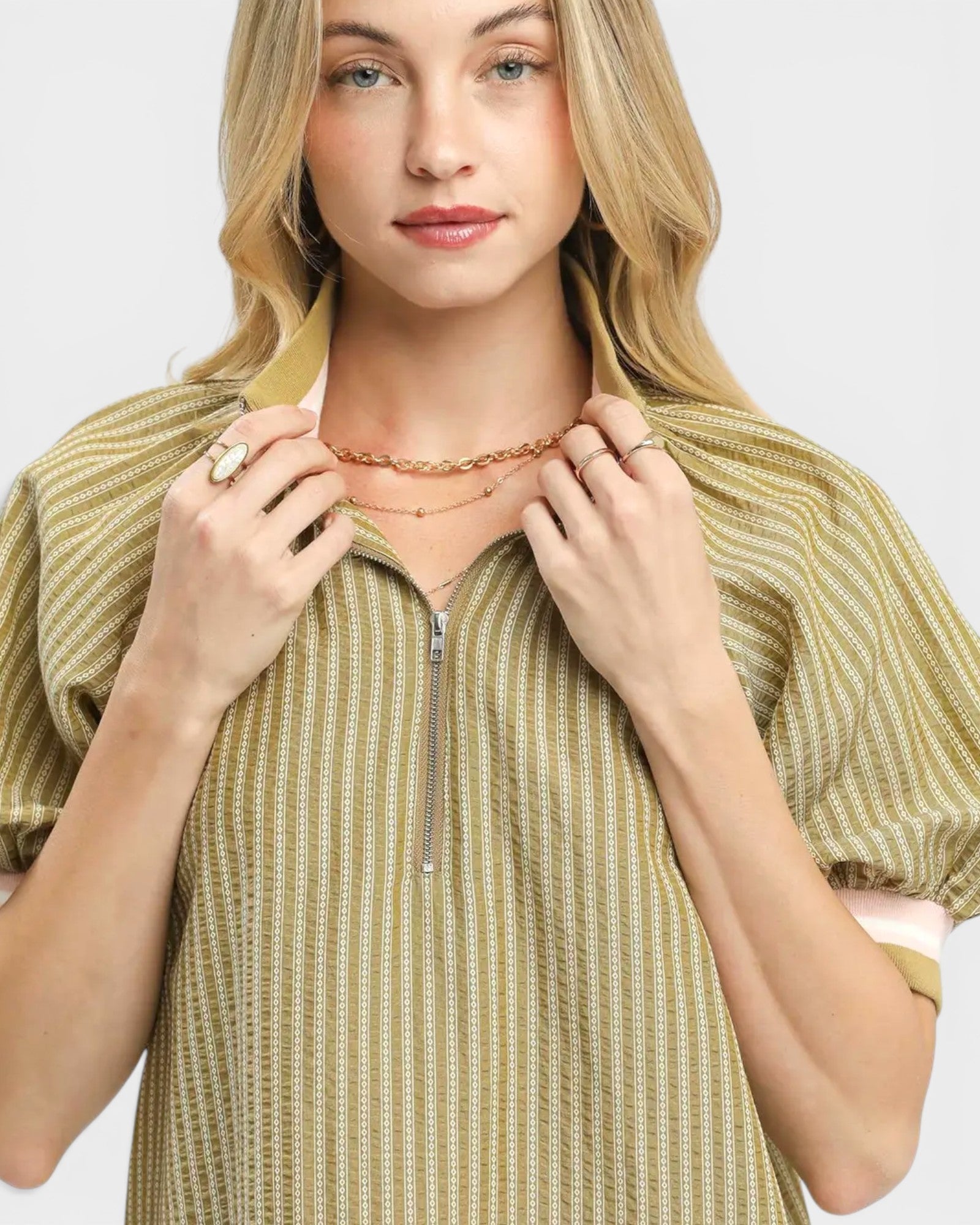 Woman wearing a patterned top and multiple necklaces on a plain background