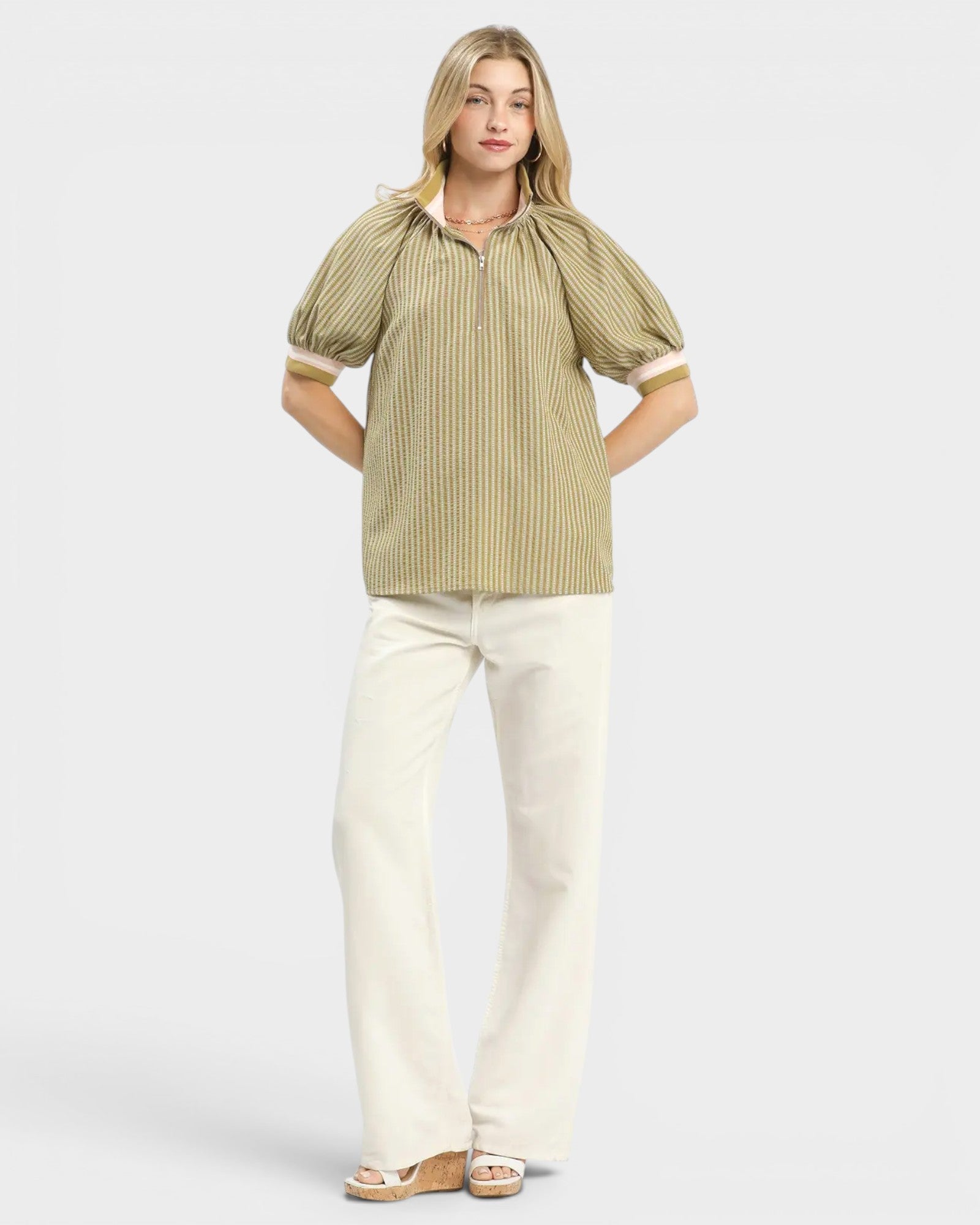 Woman wearing a striped blouse and white pants on a light background