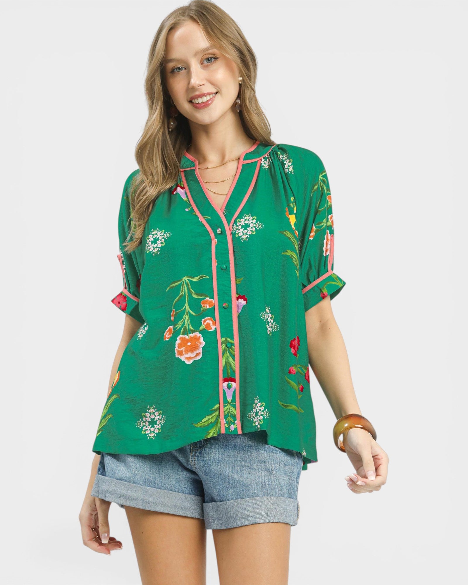 Woman wearing a green floral blouse and denim shorts on a white background