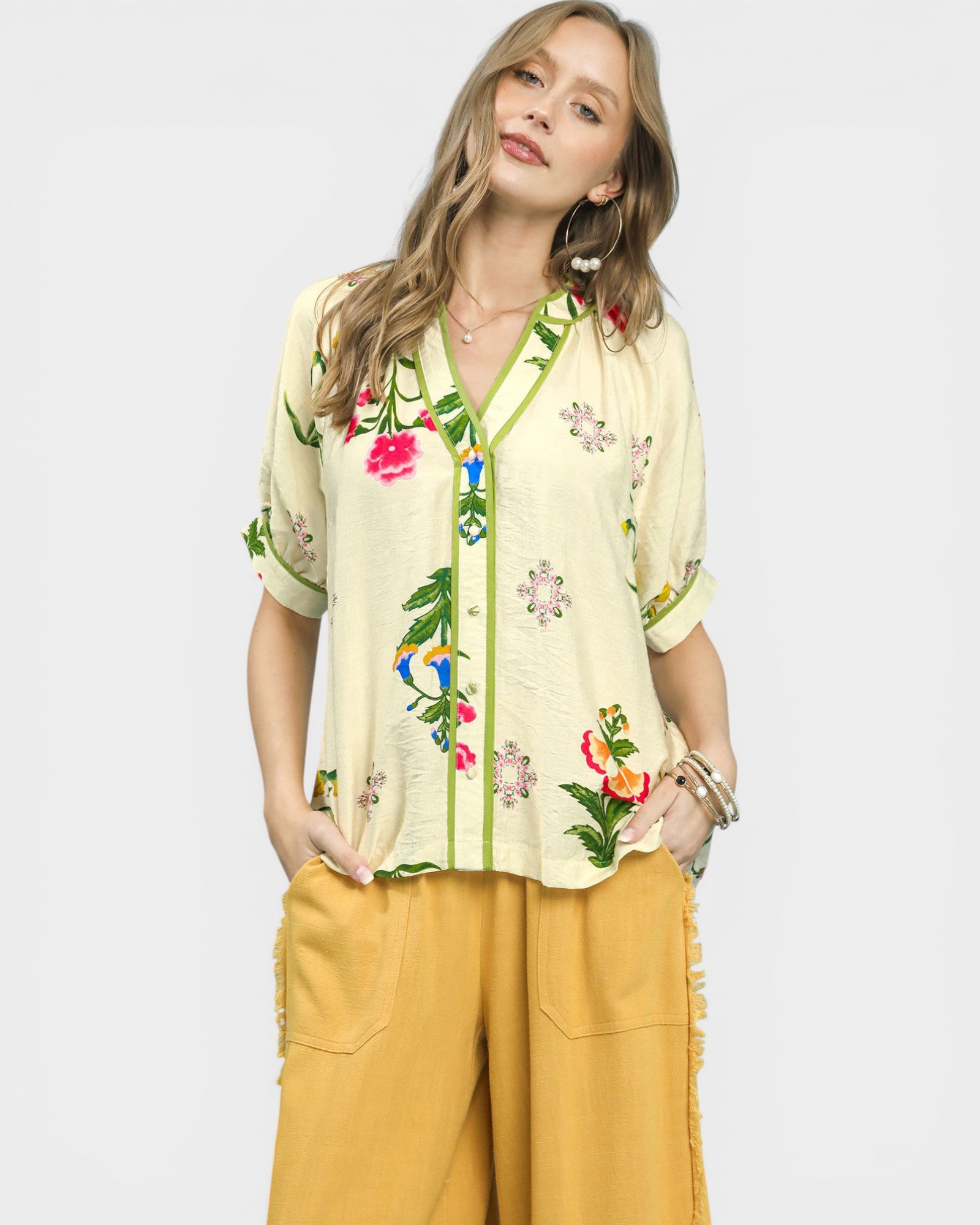 Woman wearing a light-colored embroidered top with floral designs on a plain background