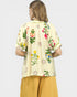 Woman wearing a cream-colored top with floral embroidery and mustard yellow pants on a white background