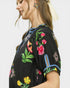 Woman wearing a black top with colorful floral embroidery on a white background