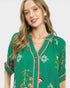 Woman wearing a green floral embroidered top on a white background