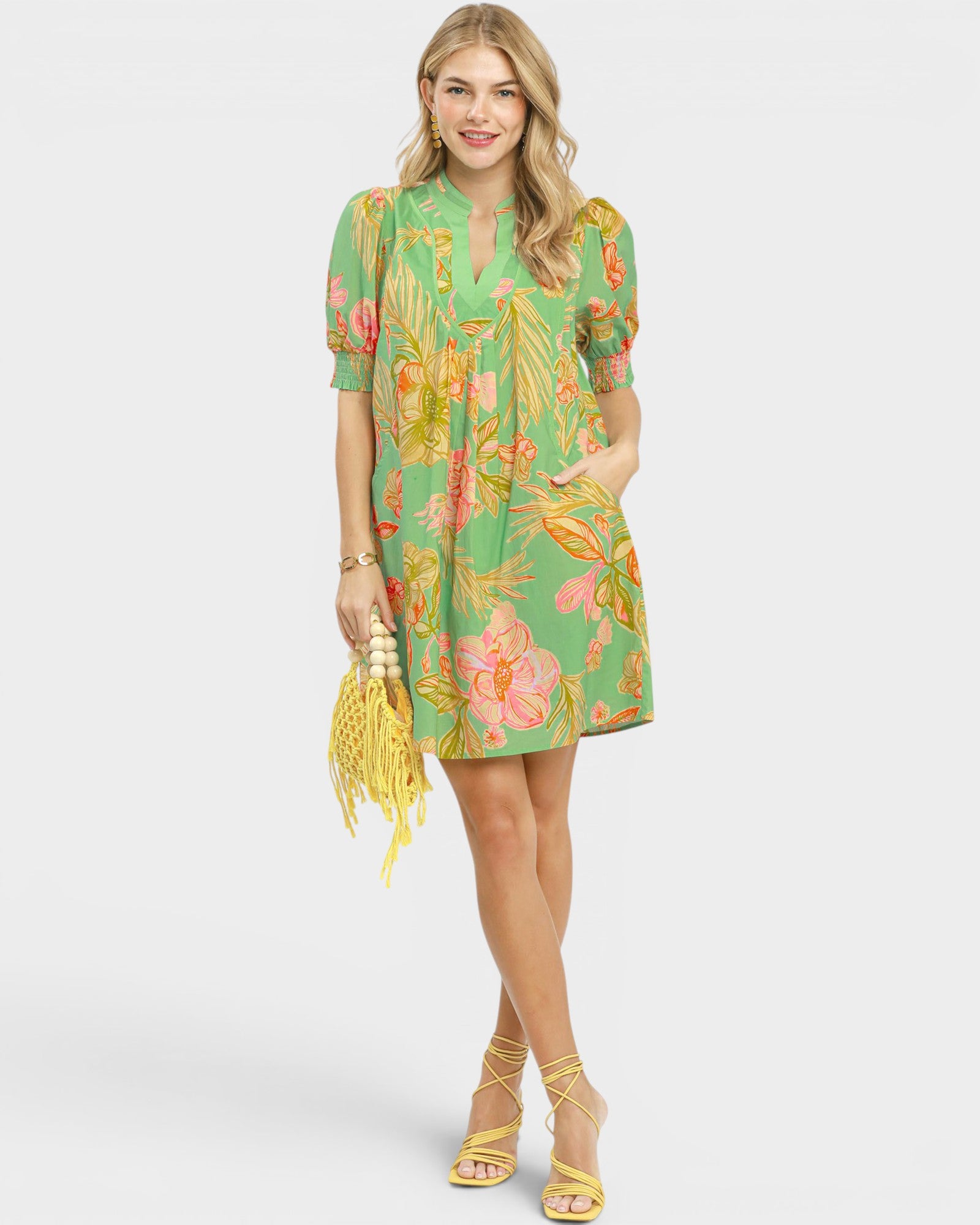 Woman wearing a green floral dress holding a yellow bag on a white background