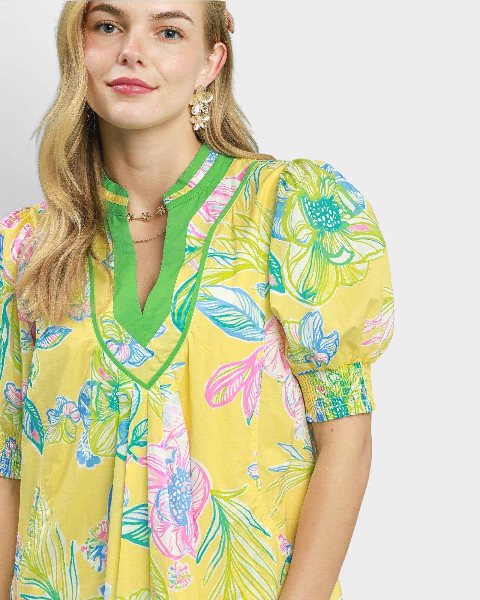 Woman wearing a yellow floral dress with green neckline against a white background