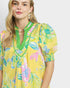 Woman wearing a yellow floral dress with green neckline against a white background