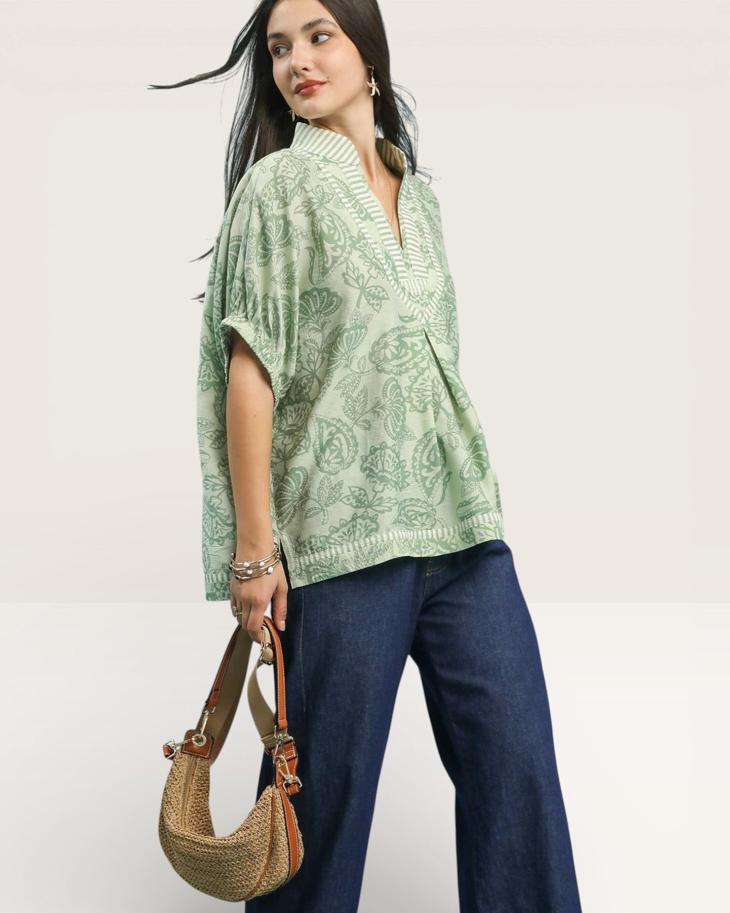 Woman wearing a green patterned poncho and holding a brown handbag on a white background