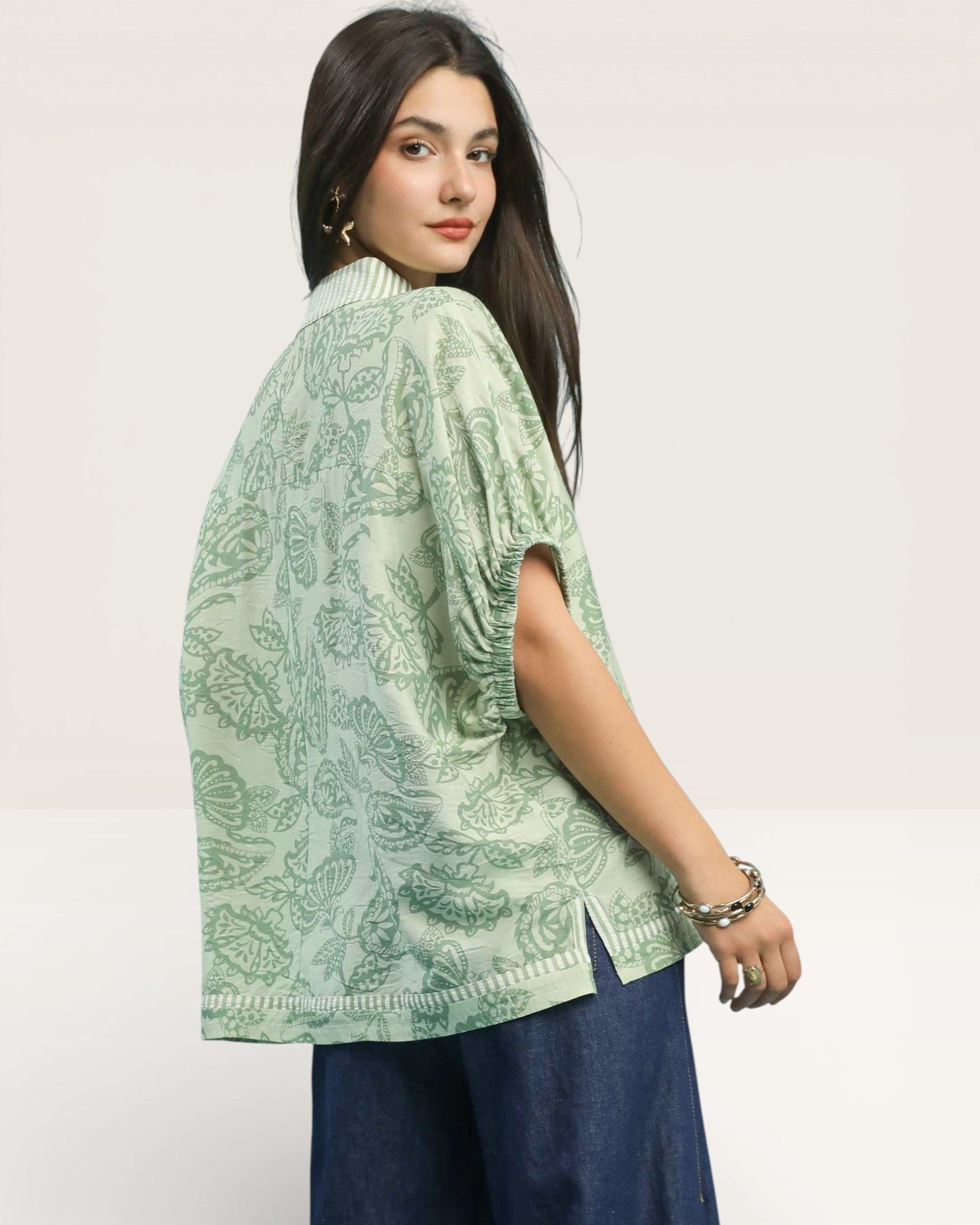 Woman wearing a light green patterned top with a plain background