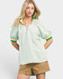 Woman wearing a light green patterned shirt with short sleeves and beige shorts on a white background