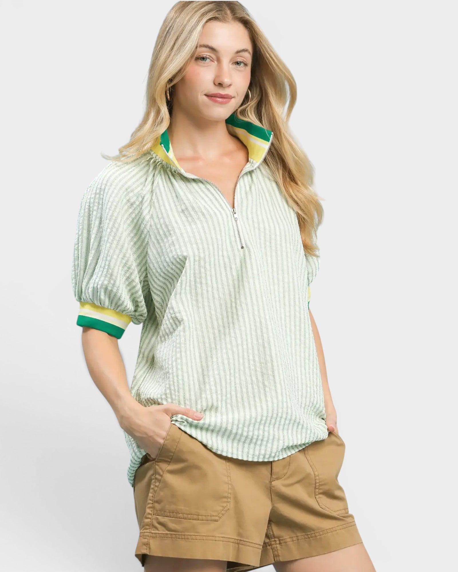 Woman wearing a light green striped shirt with yellow accents and beige shorts on a white background